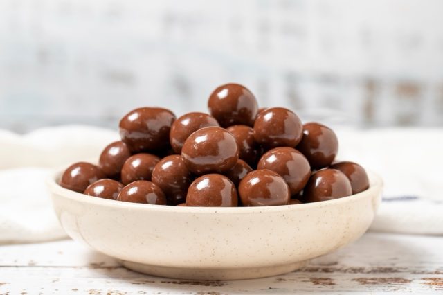 Chocolate coated hazelnut dragee. Hazelnut dragee chocolates on a white wood background. close up