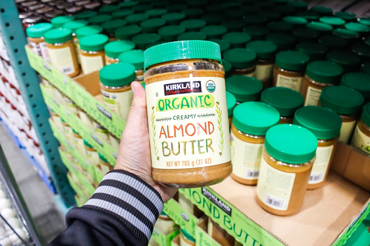 Los Angeles, California, United States - 02-08-2020: A hand holds a jar of Kirkland Signature organic creamy almond butter on display at a local Costco.