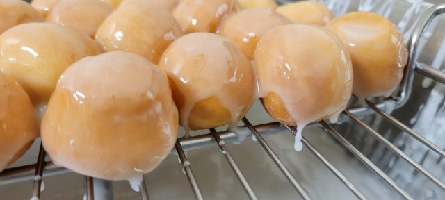 Glazed yeast munchkins dripping off rack.