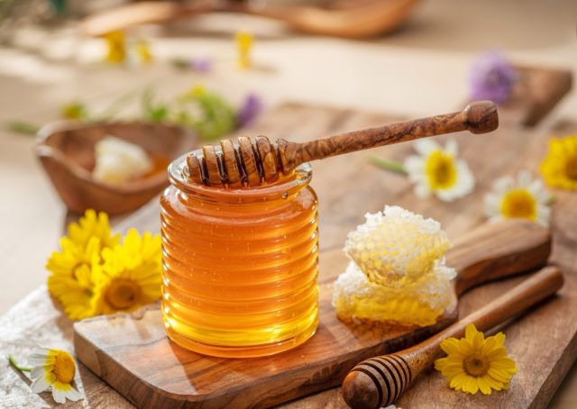 Natural organic honey in glass jar, honey dipper and honeycombs are near. Natural food background.