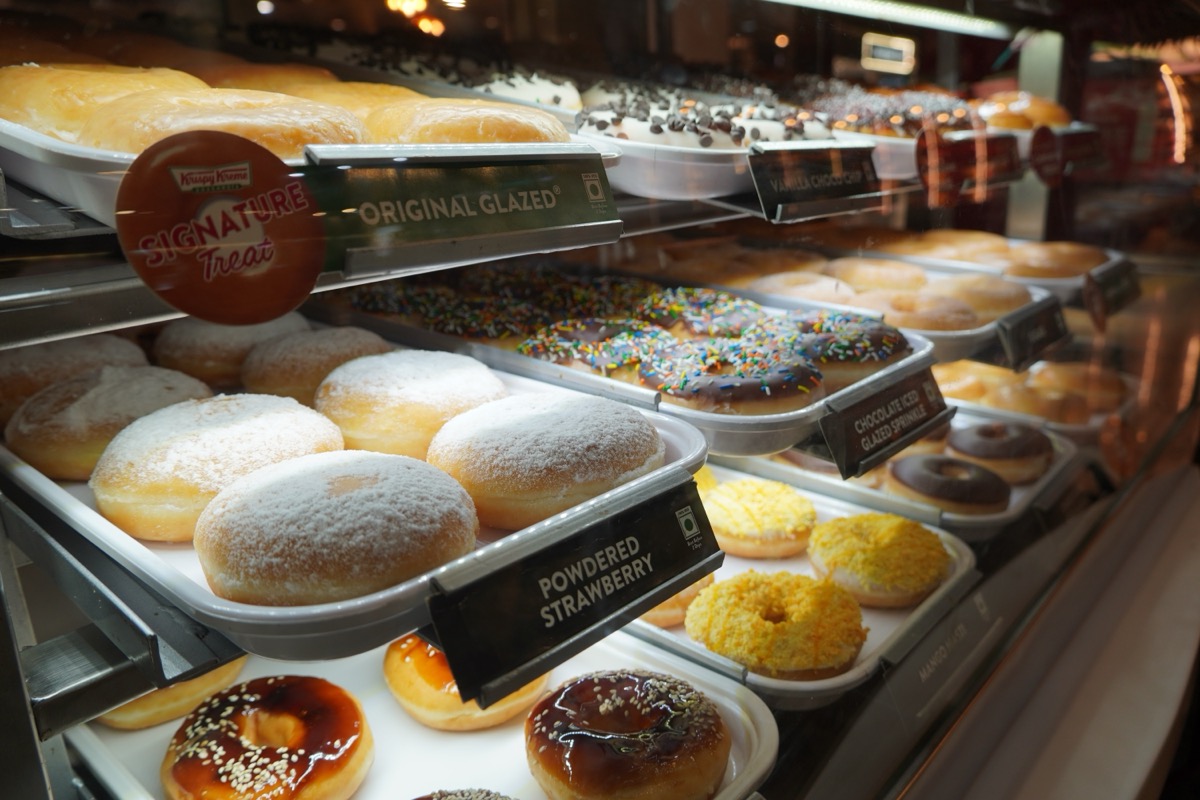 Display of delicious pastries with assorted glazed donuts in shop counter. Various donuts on shelf in Bakery. Colorful flavor donuts with coating, topping in glass showcase. Goa India - May 2021