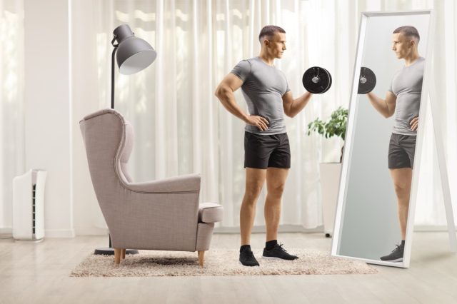 Man lifting a dumbbell and looking at a mirror at home