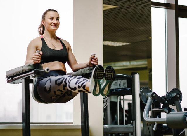 Portrait of sexy muscular girl wearing sportswear doing exercise on the bar raises his legs up, exercises on the press in the gym. Sport concept.