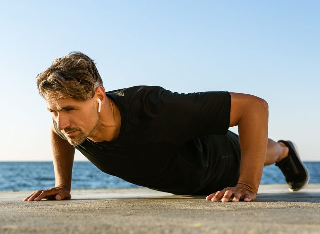 handsome adult sportsman with wireless earphones doing push ups on seashore