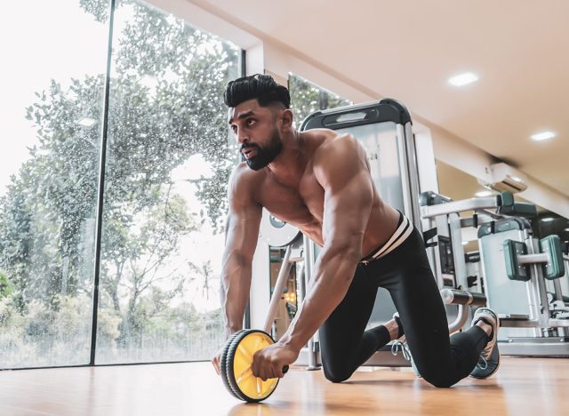 Athlete sporty man doing exercise with abs roller wheel to strengthen his abdominal muscle in gym.