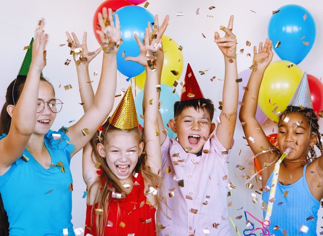 Bright, cute children celebrate a birthday. Multinational party, balloons, confetti, caps, smiles, teenagers are happy raising their hands up.