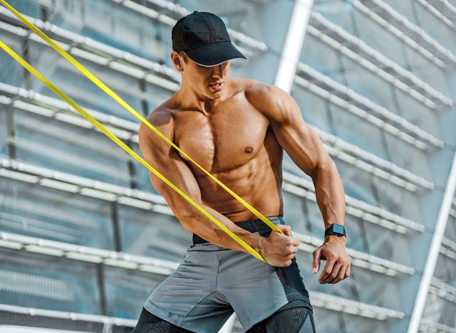 Athletic man performs exercises using resistance band. Photo of strong man training in the city. Strength and motivation