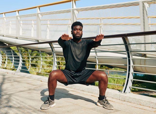 Handsome fit young Black man putting arms straight out in front of him, parallel to the ground and doing wide squats