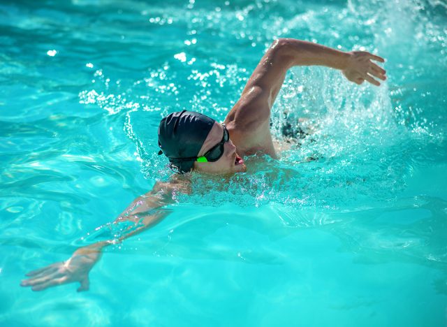 Movement in water. Man in black swimming cap floating on his side with his mouth open in pool