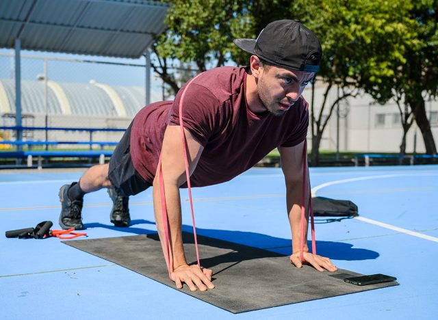 hispanic male athlete trainer working out with resistance bands, push ups and body weight training. Latin man training at a park on a sunny day for well beign