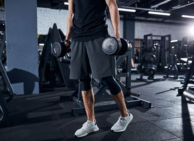 Cropped photo of a sportsman in shorts and white boots walking away with hand weights