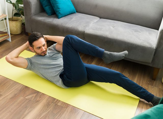 Handsome man working out and doing bicycle crunches exercises in the floor of his living room. Young man starting a cardio routine