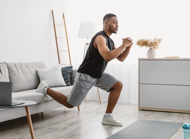 Online Training. Sporty Black Guy Doing Single-Leg Squats Near Couch Exercising At Laptop Computer During Workout At Home. Domestic Male Fitness And Sporty Lifestyle. Side View