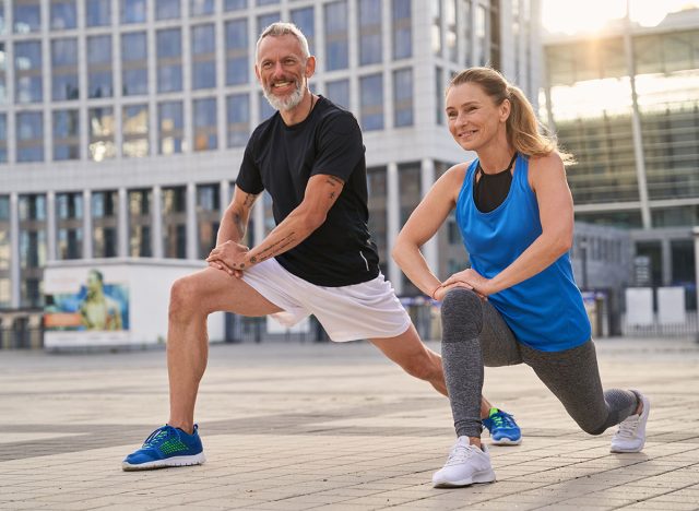 Cheerful sporty middle aged couple, man and woman warming up, getting ready for running together in the city on a summer day