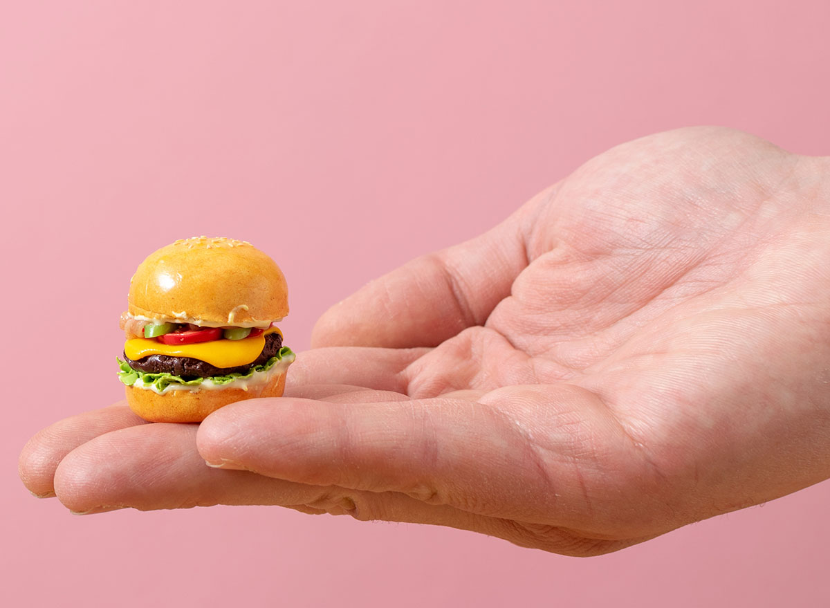 Miniature burger in hand on a pastel pink background. Minimalistic food concept.