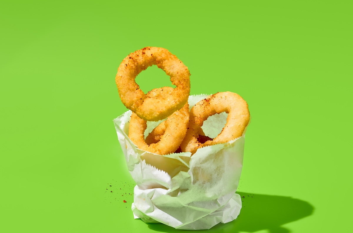 Fried,Onion,Rings,In,Paper,Bag,On,Green,Background.,Flying