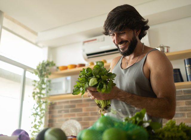 Happy and healthy young man meal prepping whole vegetarian meal in the kitchen. High quality photo. Feel good, healthy and health concept.