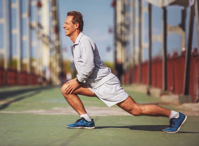 Side view of handsome middle aged man in sports uniform warming up, doing lunges and smiling during morning run