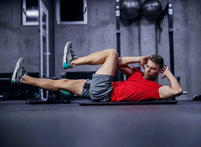 Sportsman doing bicycle lateral crunch workout at the gym. A hot male person in a fitness club doing sit-up exercises. Fitness goal, sport lover, legs extension