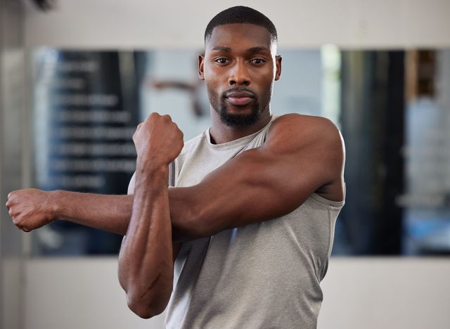 Gym portrait and black man stretching arms for bodybuilder fitness and muscle warm up with focus. Training, wellness and athlete man workout preparation for exercise lifestyle at health club.