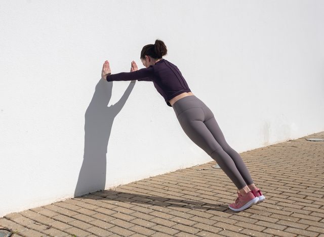 Sporty woman doing press ups against a white wall outside, wall push up. 