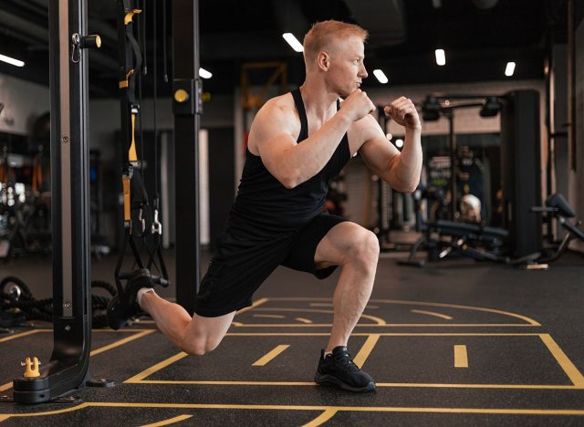 Strong sportsman doing bulgarian lunges in a gym with TRX