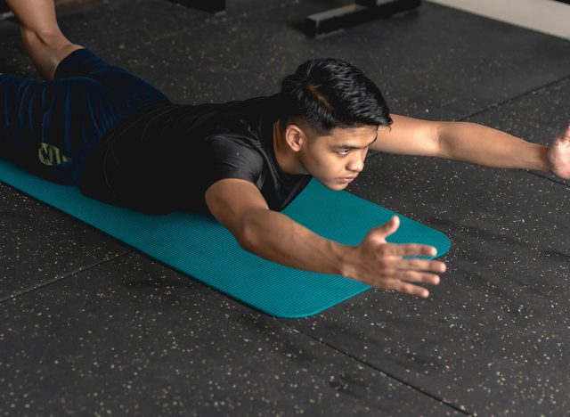 A young handsome asian man does superman back extension exercises while lying prone on a mat at the gym. Training and strengthening lower back muscles.