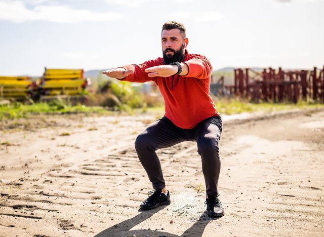 Young man is exercising outdoor. He is doing squats.