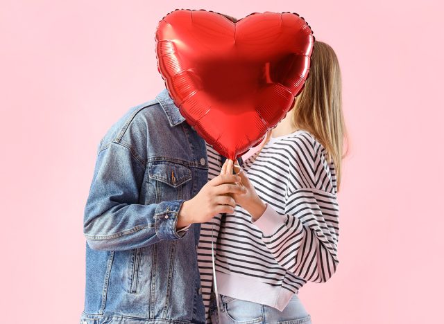 Happy young couple with beautiful heart-shaped balloon on pink background. Valentine's Day celebration