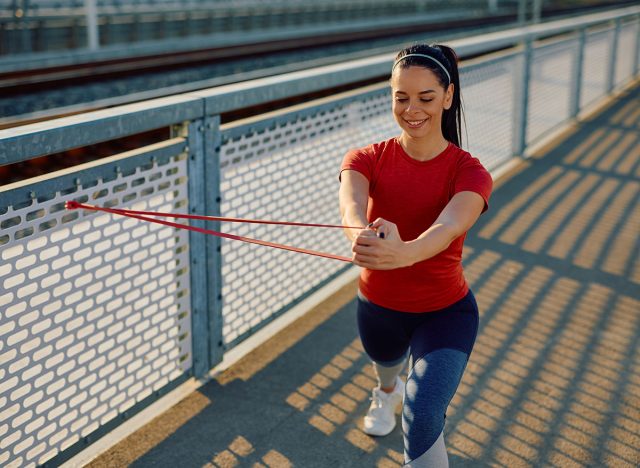 Athletic woman using resistance band while strengthening her arms during outdoor workout. Copy space.