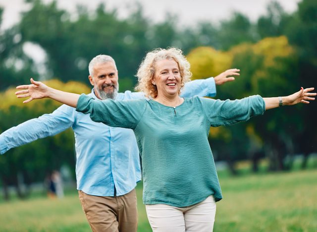 Happy active mid aged adult couple having fun walking and balancing and bonding in park or nature outdoors, healhty active mature people exercise concept