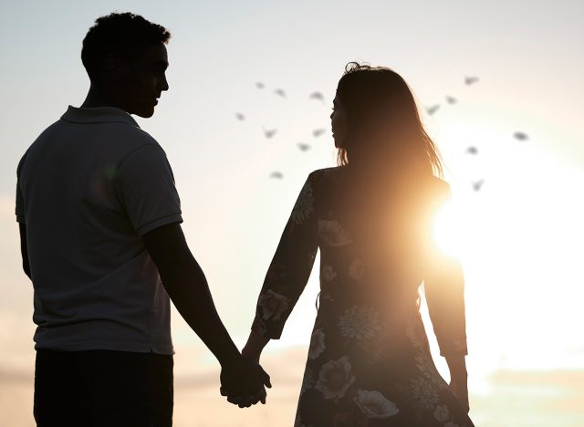 Couple, silhouette and holding hands at romantic, destination, holiday or honeymoon in summer at sunset on vacation on date. Woman, man and relationship in love or together, memory and travel on trip