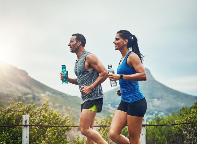 Couple, people and smile with running for fitness or training, support and love in Brazil. Workout, exercise and outdoor with jogging for health, wellness and wellbeing in sunset with lens flare