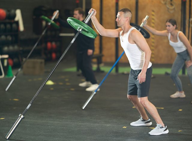 Focused man performing single arm landmine press using barbell 