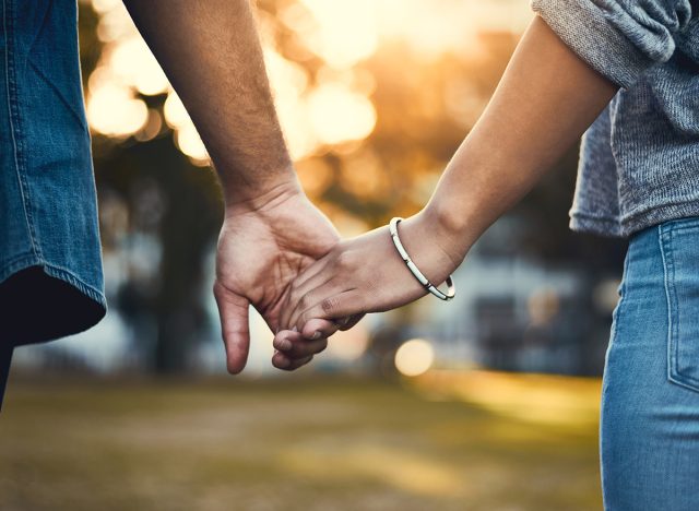 Couple, back and holding hands outdoor for love, relationship and date together with loyalty. Man, woman and commitment as romantic walking with trust, support and care in street for happiness