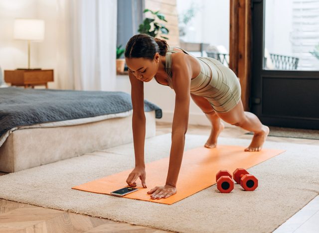 Portrait of sporty African American woman turning on the timer on smartphone, doing plank exercise at home. Healthy lifestyle, sport concept