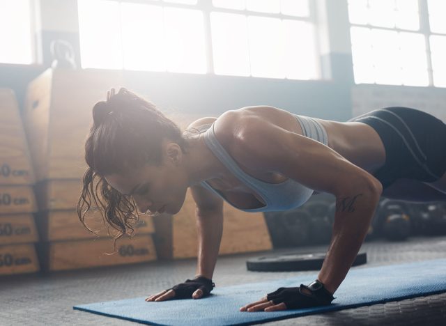 Shot of young woman doing push-ups at the gym. Muscular female doing pushups on exercise mat at gym. Female exercising on fitness mat at gym.