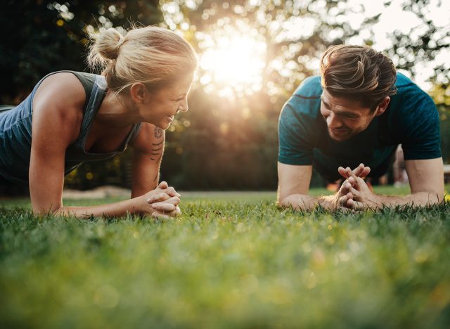 Fit young man and woman exercising in park. Smiling caucasian couple doing core workout on grass. Morning workout. 