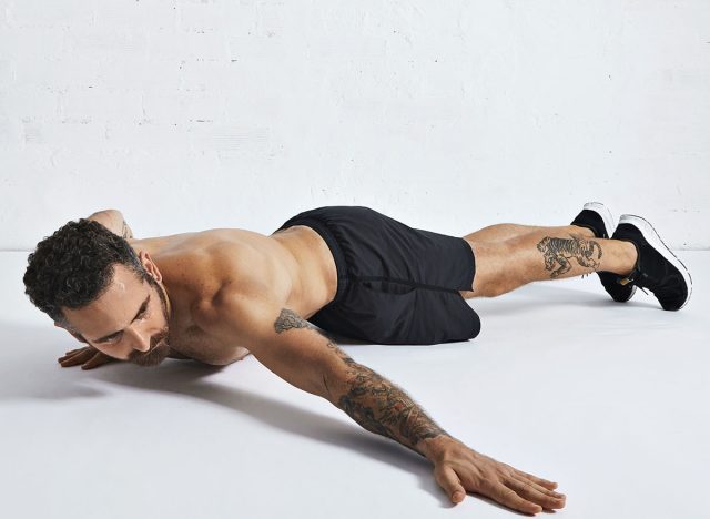 Strong brutal tattoed and ripped male athlete shows how to do archer push-ups, isolated on white spacious room, low position on right hand