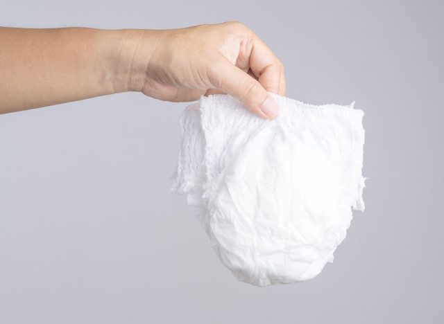 Hand holding used baby diaper on white background