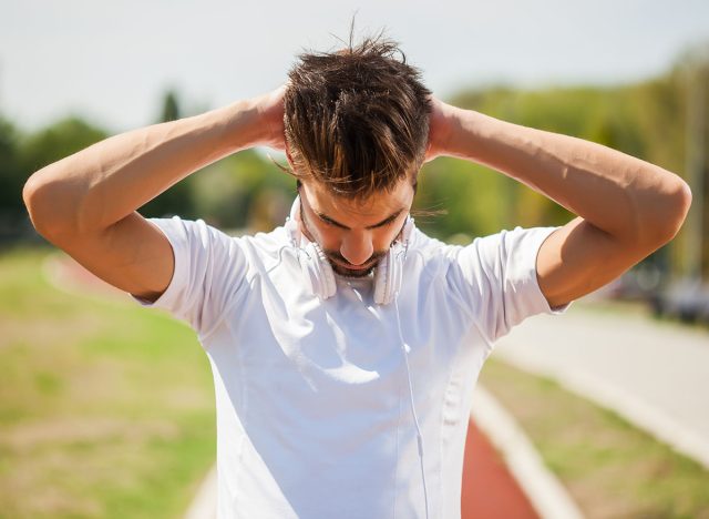 Young man is exercising on sunny day. He is stretching his body.