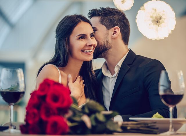 Beautiful loving couple is spending time together in modern restaurant. Attractive young woman in dress and handsome man in suit are having romantic dinner. Celebrating Saint Valentine's Day.