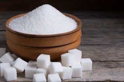 Granulated sugar in a wooden cup, a scattering of refined sugar cubes