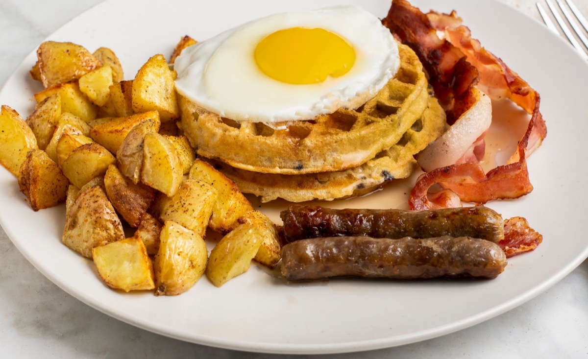 fried egg on waffles seved with homefries, sausages, and bacon