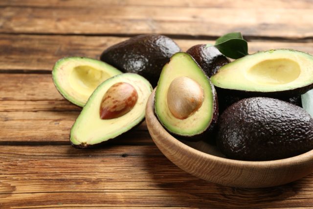 Whole and cut avocados on wooden table, closeup