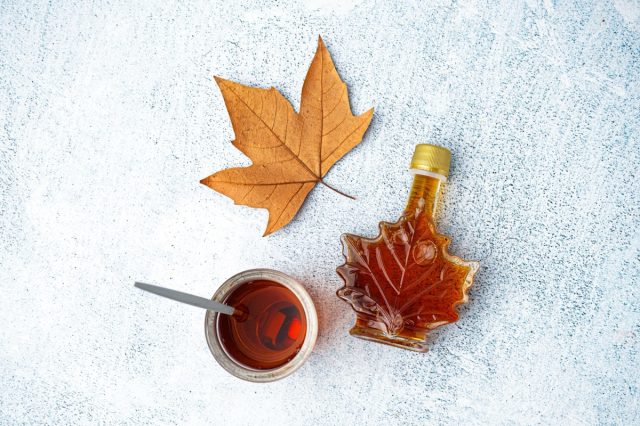 Bottle and glass of tasty maple syrup on grey background