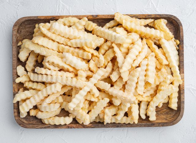 Frozen crinkle oven fries set, on wooden tray, on white background, top view flat lay