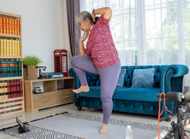 Senior woman exercise with standing oblique crunch or side crunch, she watch training online in tablet during workout, standing oblique crunch