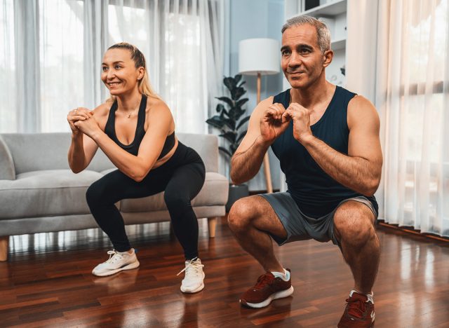 Athletic and sporty senior couple engaging in leg day training session with squat together at home exercise as concept of healthy fit body lifestyle after retirement. Clout