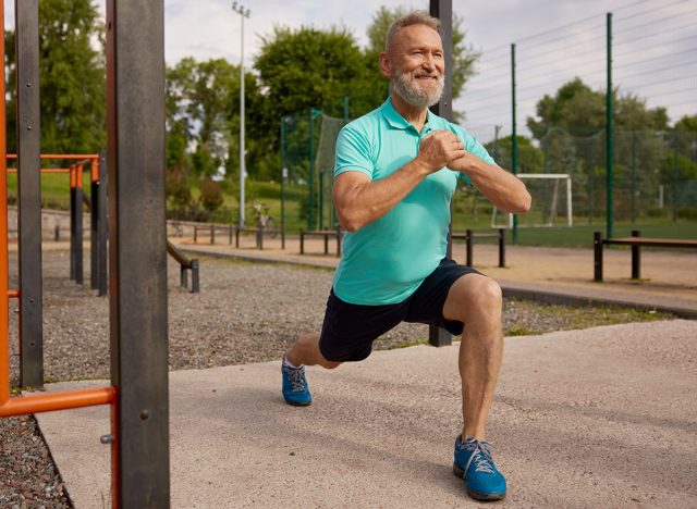 Senior man doing lunges physical exercises at sport field outdoors